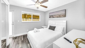 A bedroom with a bed, a nightstand, a white desk, a ceiling fan, a window, and a painting on the wall. - Victoria Park Getaway! 1 Mile to Beach & Las Olas! (Fort Lauderdale)