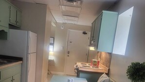 Una cocina compacta con comedor, una mesa pequeña con tazas, un refrigerador y una planta en maceta.