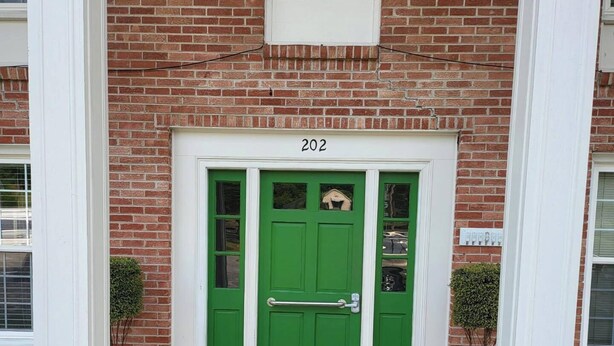 Un edificio de ladrillo con una puerta verde, el número 202, y una pequeña ventana arriba.