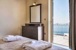 A hotel room with a bed, a dresser, a mirror, and a balcony with a view of the sea.