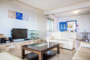 A modern living room with a flat-screen TV, a glass coffee table, and a white leather sofa.