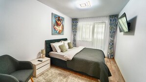 A bedroom with a bed, a chair, a nightstand, a painting, and a TV on the wall.