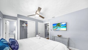 Ein Schlafzimmer mit Bett, Deckenventilator, einem Strandbild und einem Kleiderschrank.