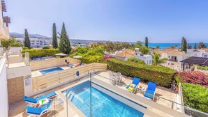 Un área de piscina en la azotea con varias piscinas, sillas de descanso y vistas al mar.