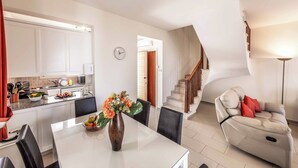 Una cocina moderna con armarios blancos, una mesa de comedor con sillas, un florero con flores y un sofá en la sala de estar.