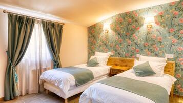 Una habitación con dos camas, cabeceros de madera, papel tapiz floral y una ventana con cortinas.