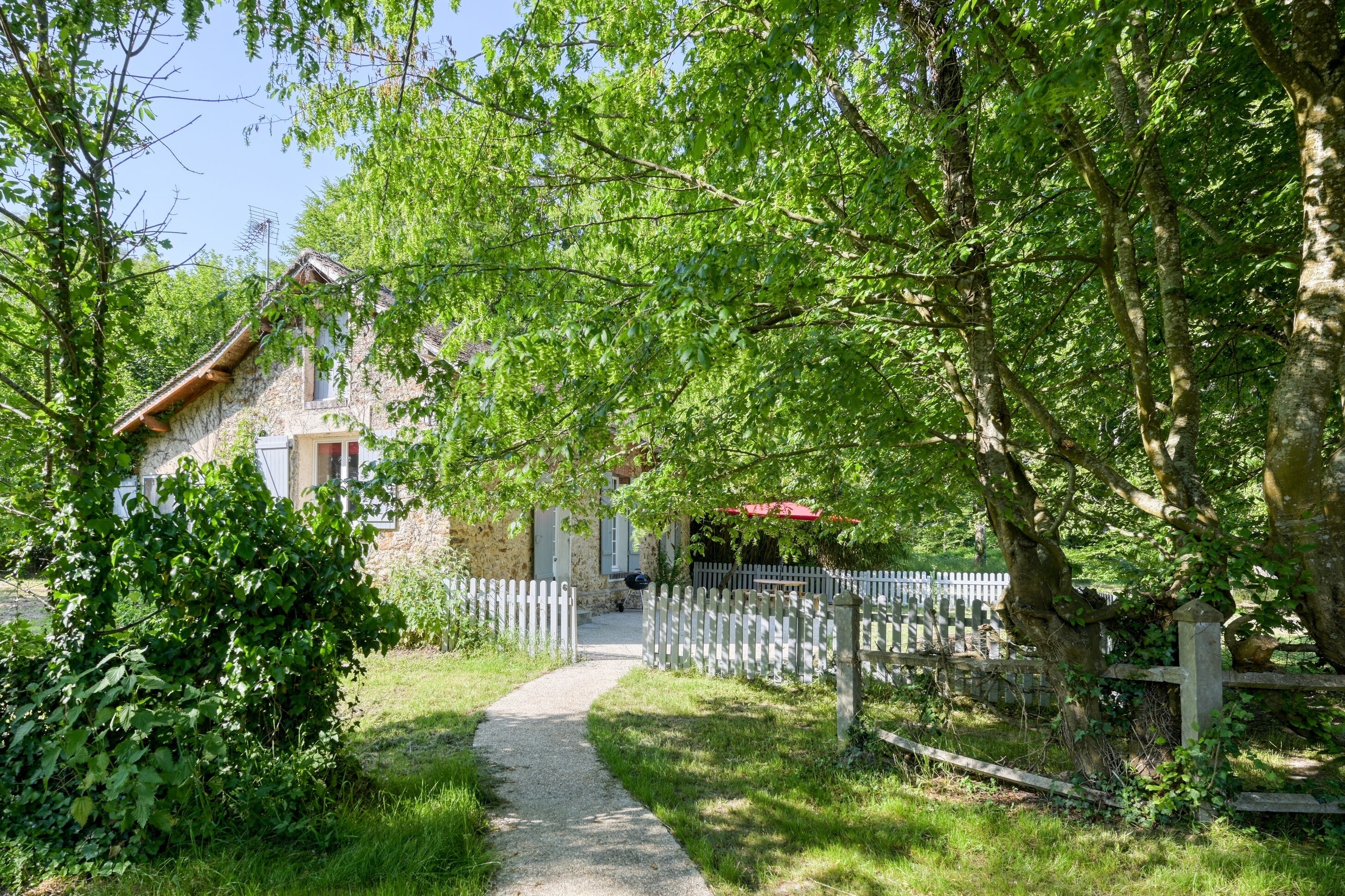 A stone house with a gravel path leading to a white picket fence.
