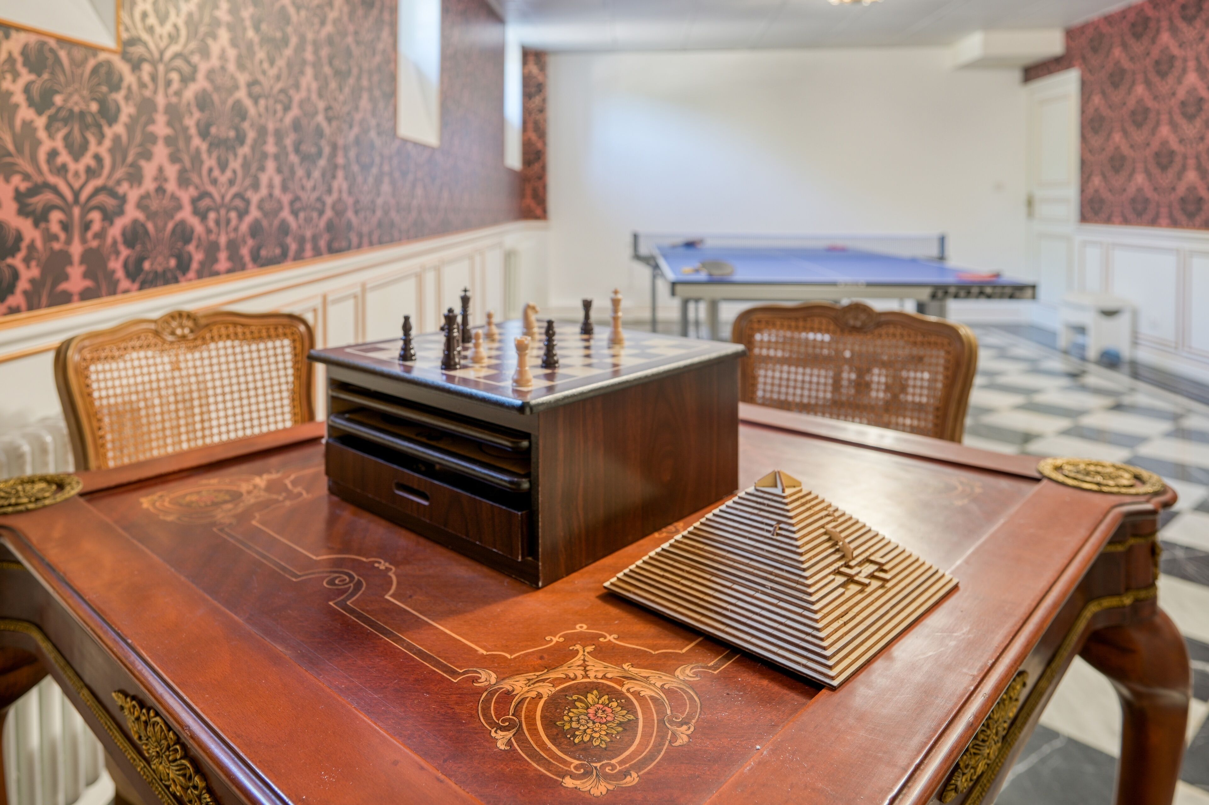 A wooden table with a chessboard, a checkered floor, and patterned wallpaper.