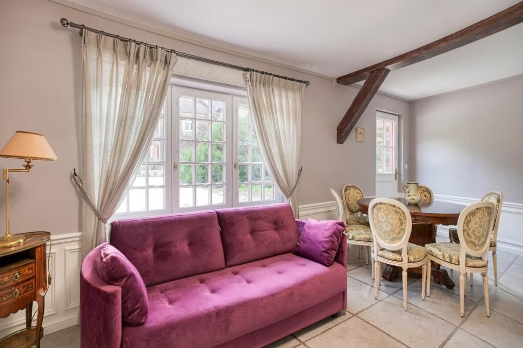 Una habitación con un sofá púrpura, una mesa de madera con sillas, y una lámpara.