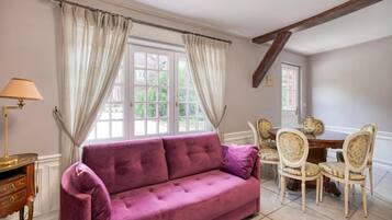 A room with a purple sofa, a wooden table with chairs, and a lamp.
