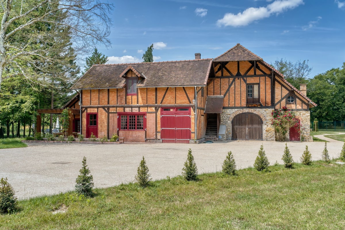 Il s’agit d’un bâtiment traditionnel à colombages, doté d’une entrée en arc de pierre, d’une porte de garage rouge et d’une allée gravillonnée.