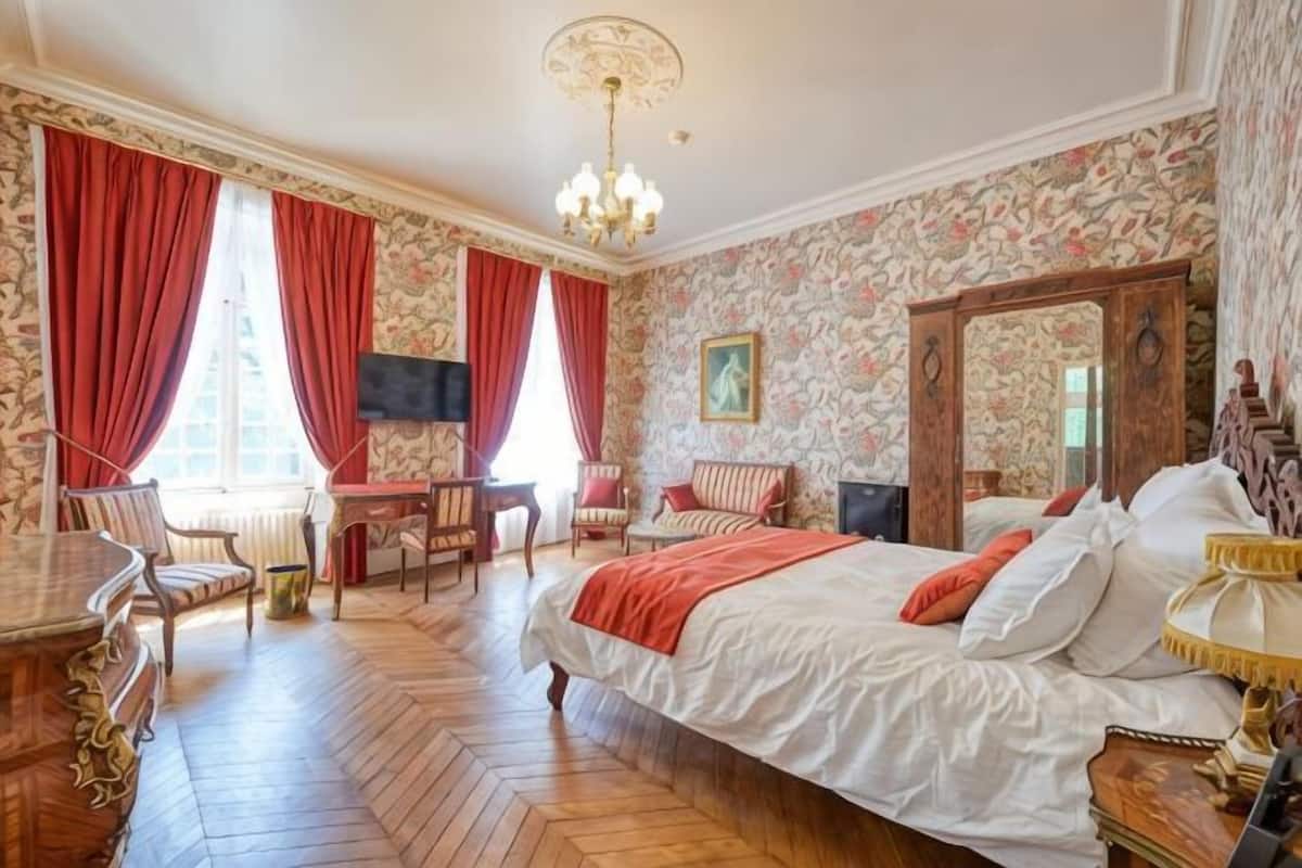Une chambre d’hôtel avec un grand lit, un bureau, deux chaises, une télévision et un lustre.