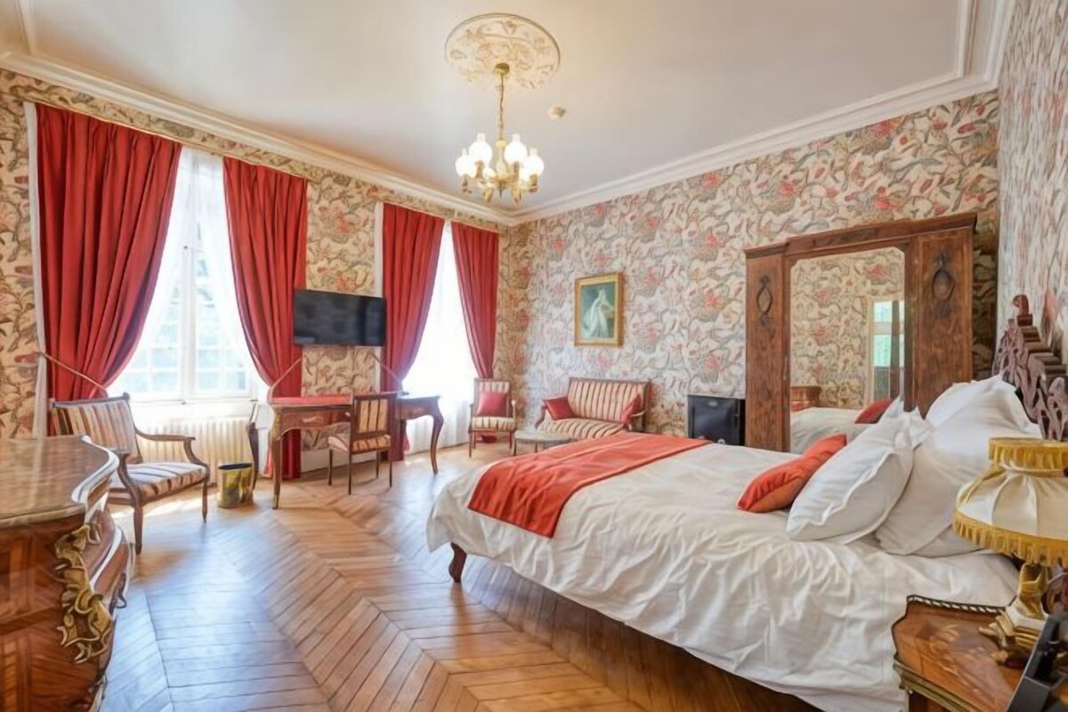 Una habitación de hotel con una cama grande, un escritorio, dos sillas, un televisor y una araña.