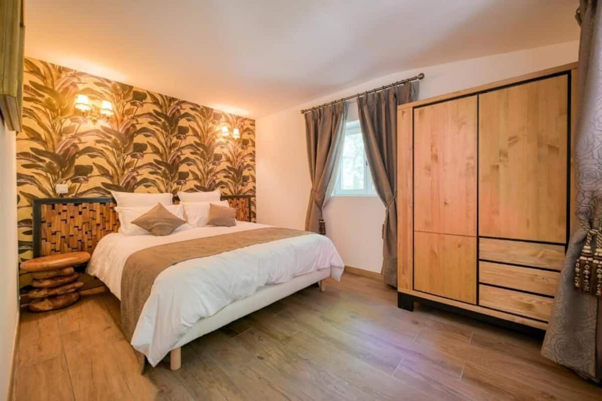 Une chambre à coucher avec une tête de lit en bois, un lit avec une literie blanche, une armoire et une fenêtre avec des rideaux.