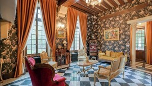 Een kamer met een zwart-wit betegelde vloer, een rode fauteuil, een bank en een tafel met een klok.