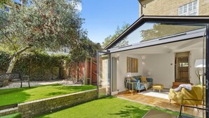 Et moderne hus med en glasindhegnet terrasse, en velplejet græsplæne og et hyggeligt interiør med en sofa og et bord.