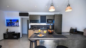A modern kitchen with a central island, bar stools, a flat-screen TV, and a fruit bowl. - Beautiful 1-bed Apartment in Pobrezje-dubrovnik (Dubrovnik)