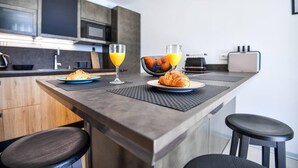A modern kitchen with a central island, two barstools, and a breakfast setting with croissants and orange juice. - Beautiful 1-bed Apartment in Pobrezje-dubrovnik (Dubrovnik)