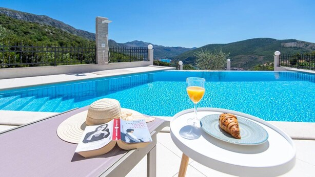 A poolside setting with a book, a hat, a glass of orange juice, and a croissant on a table. - Beautiful 1-bed Apartment in Pobrezje-dubrovnik (Dubrovnik)