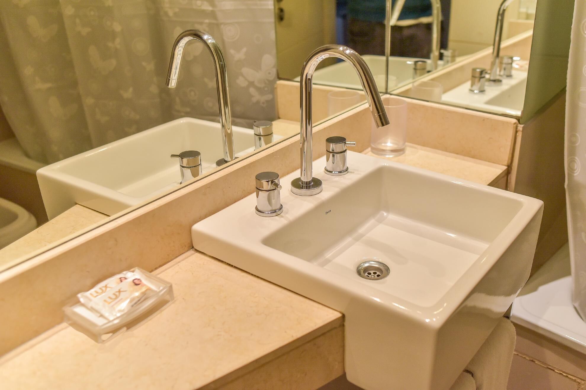 A bathroom with two sinks, each with a mirror above. There are two faucets, a soap dispenser, and a drain.