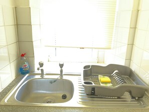 A kitchen with a stainless steel sink, a dish rack, and a bottle of Fairy dish soap. - Immaculate 1-bed Apartment in Largs (Largs)