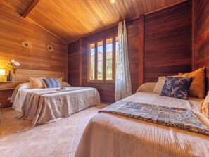 A cozy cabin-style bedroom with two beds, wooden walls, a large window with curtains, and a small table with a lamp and flowers. - Tropical 2 by Interhome (Deltebre)