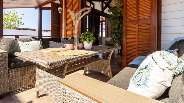 Un espacio al aire libre con mobiliario de mimbre, una mesa de madera y plantas en macetas.