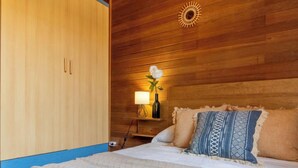 Habitación de hotel con pared de madera, cama con almohadas estampadas, mesita de noche con lámpara y decoración de estrella de mar en la cama.
