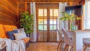 Una habitación acogedora con techo de madera, un sofá con cojines, una mesita con sillas y un televisor.