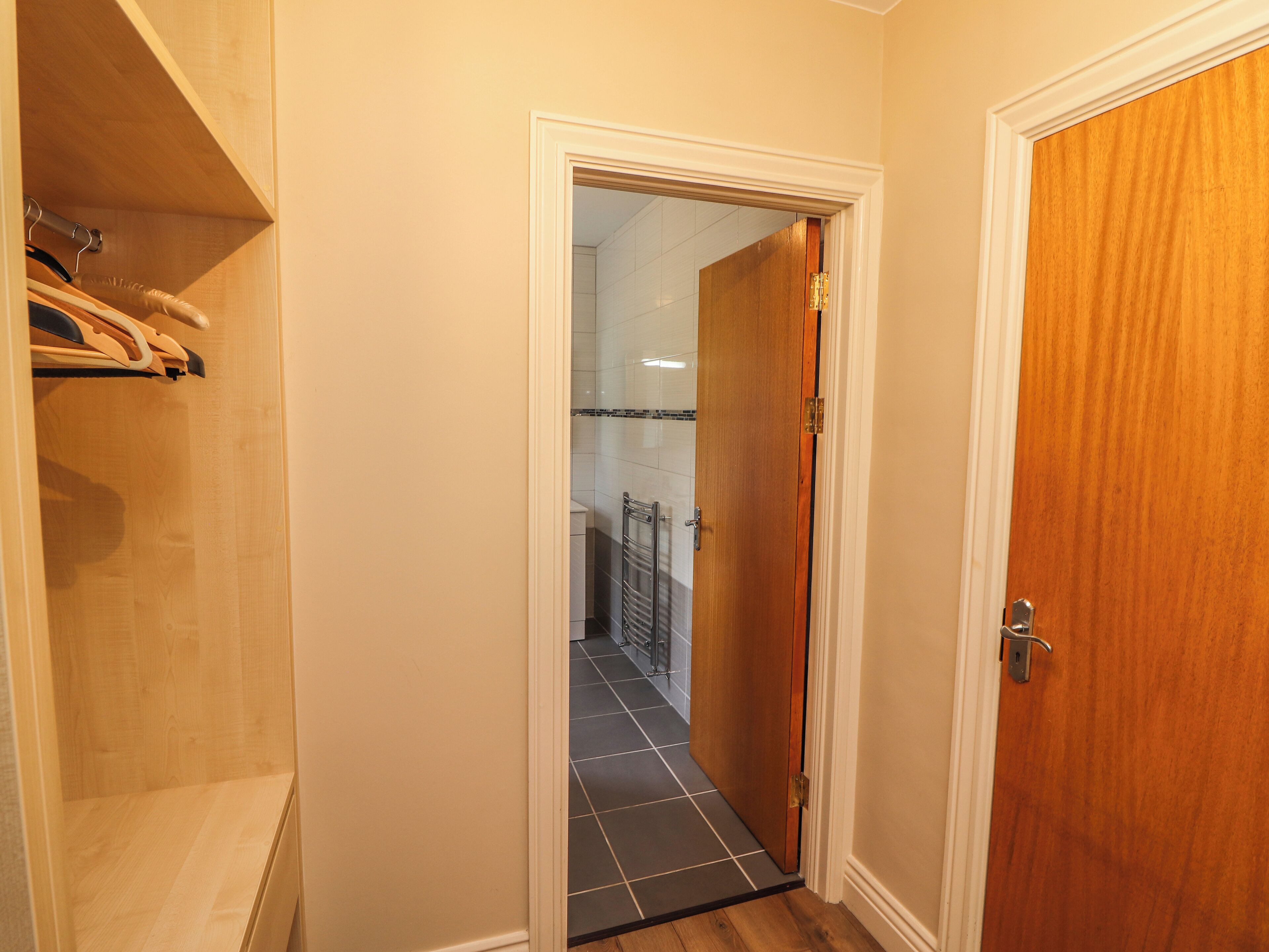 A hallway with a wooden door, a tiled floor, and a wooden closet with hanging clothes.