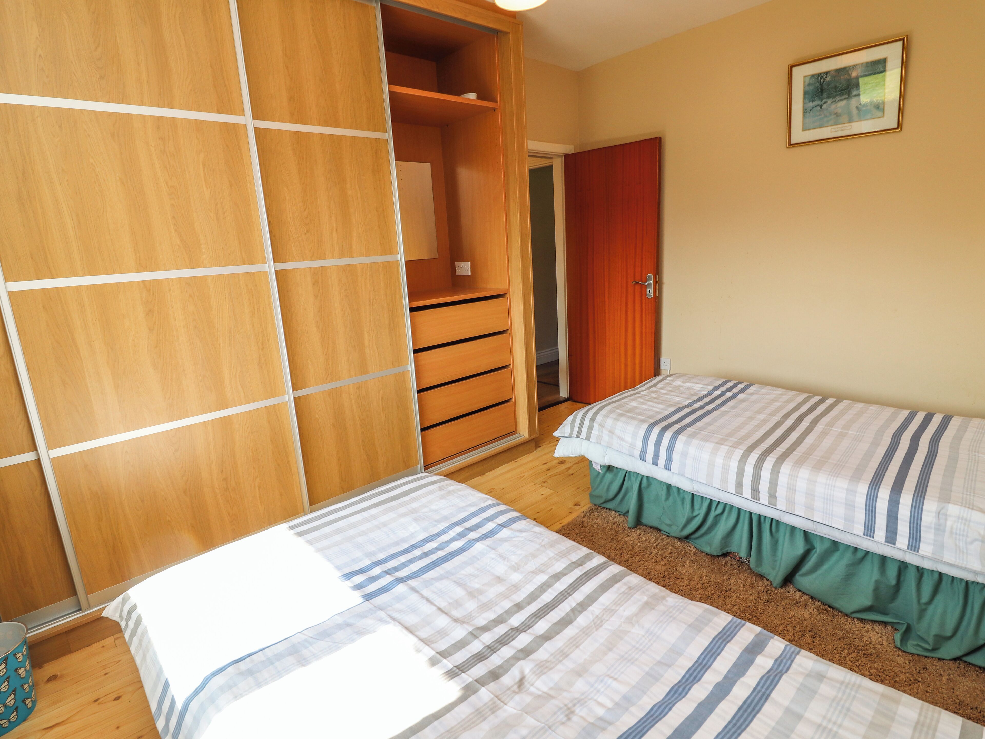 A bedroom with two beds, wooden wardrobe, and a door leading to another room.