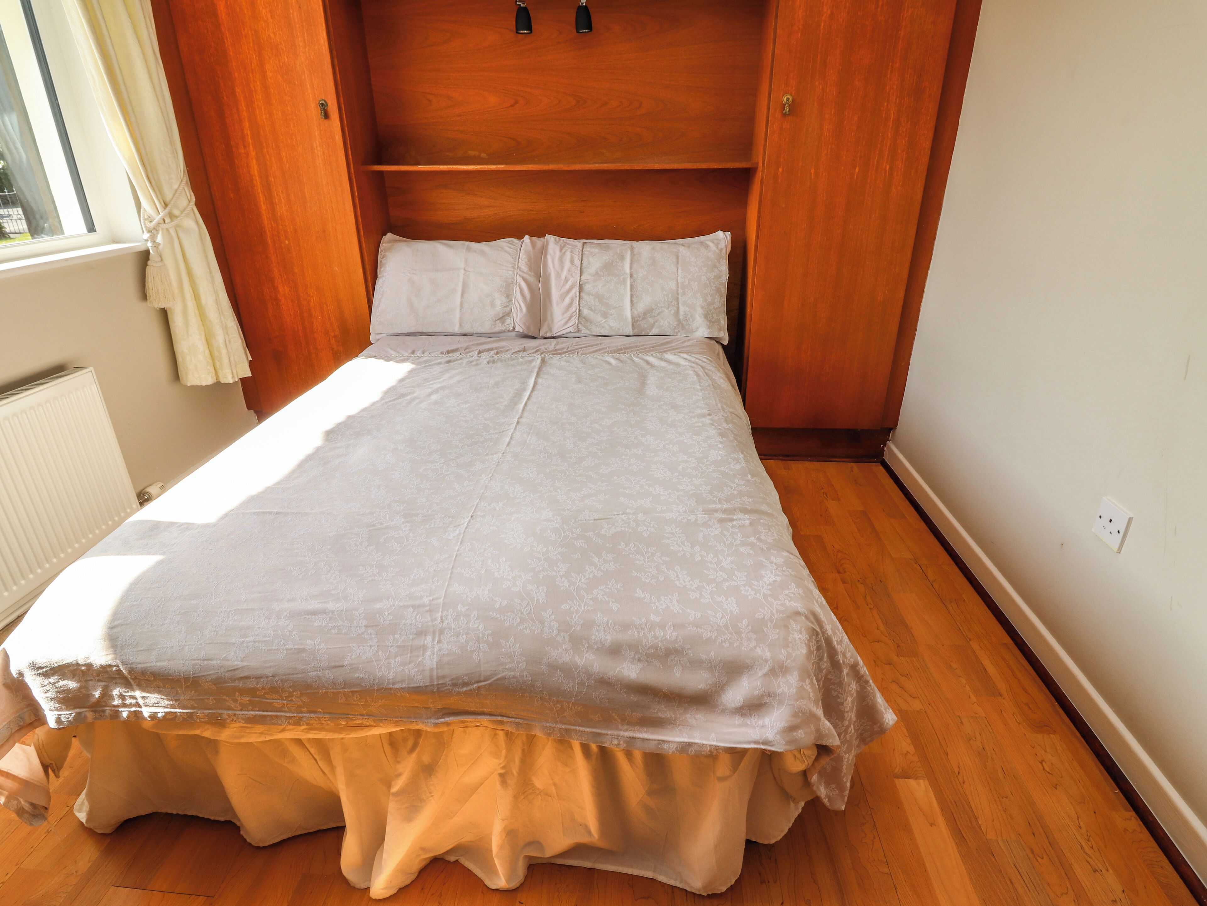A bedroom with a bed, wooden headboard, and a window with curtains.