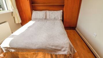 A bedroom with a bed, wooden headboard, and a window with curtains.