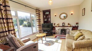 A living room with a sofa, armchair, TV, fireplace, and a view through the window. - Gap of Dunloe (Killarney)