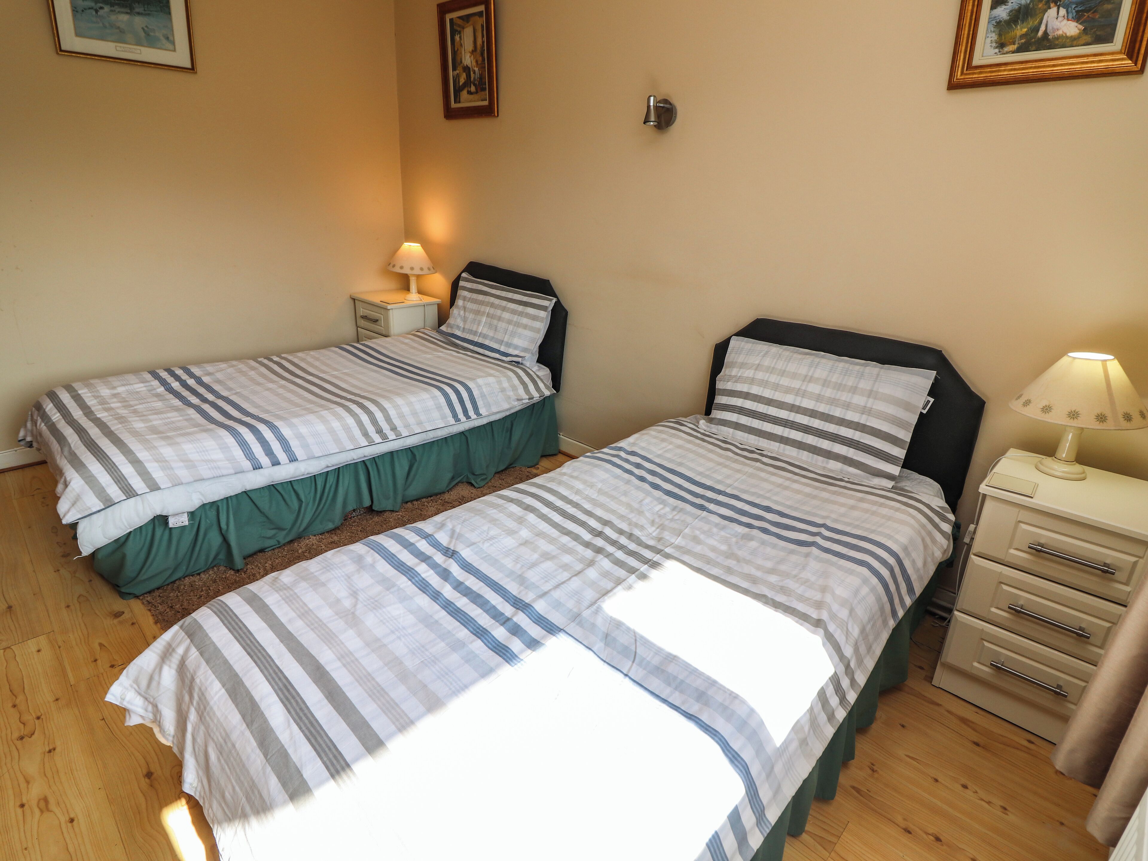 A bedroom with two single beds, a nightstand with a lamp, a dresser, and a framed picture on the wall.