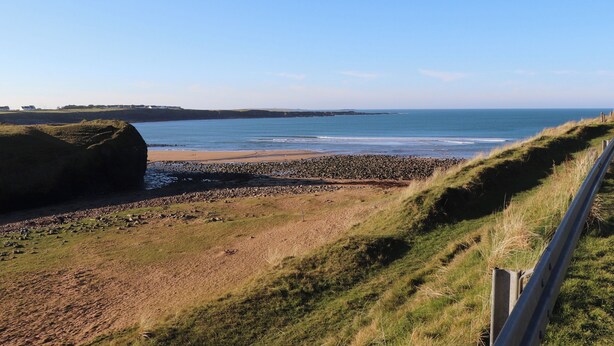 A coastal landscape with a sandy beach, rocky outcrops, and a grassy area. - Mullagh Road (Miltown Malbay)