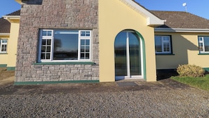 A two-story house with a stone facade, a large arched entrance, and a small satellite dish on the roof. - Mullagh Road (Miltown Malbay)