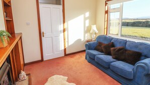A room with a blue sofa, a white door, a lamp, and a view of the outdoors. - Mullagh Road (Miltown Malbay)