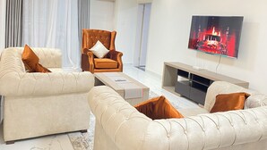 Una sala de estar moderna con un sofá beige, un sillón marrón, un televisor de pantalla plana montado en la pared y una mesa de centro con diseño de mármol.