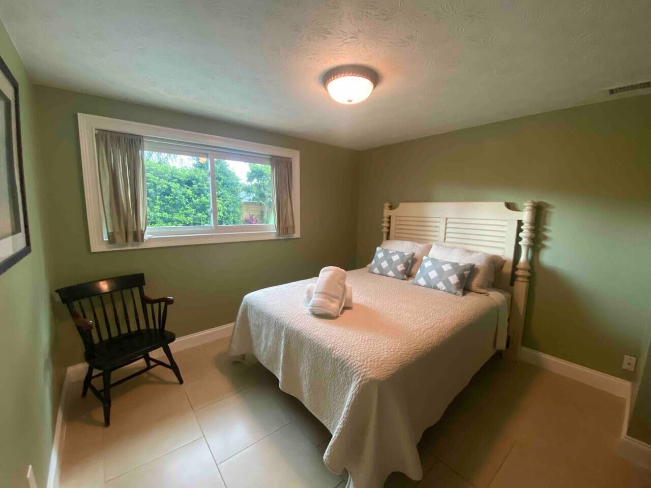 Une chambre à coucher avec un lit, une chaise, une fenêtre et un luminaire au plafond.