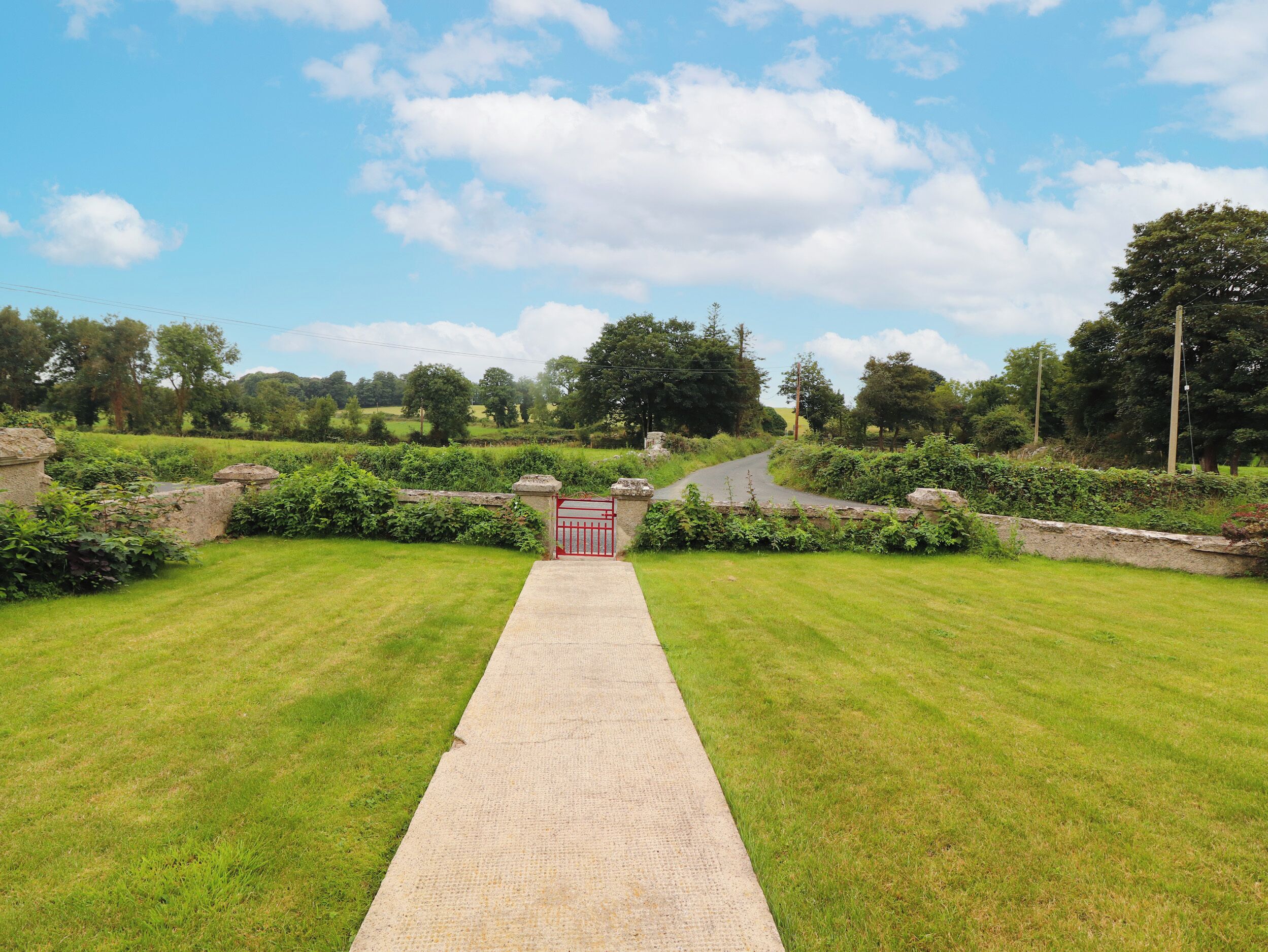 A pathway leading to a gated entrance surrounded by lush greenery and stone walls.