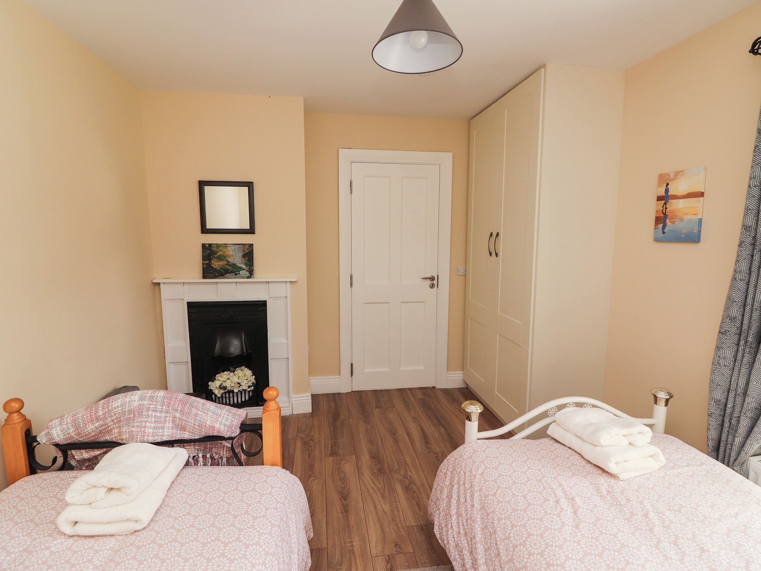 A bedroom with two beds, a fireplace, a door, and a painting on the wall.