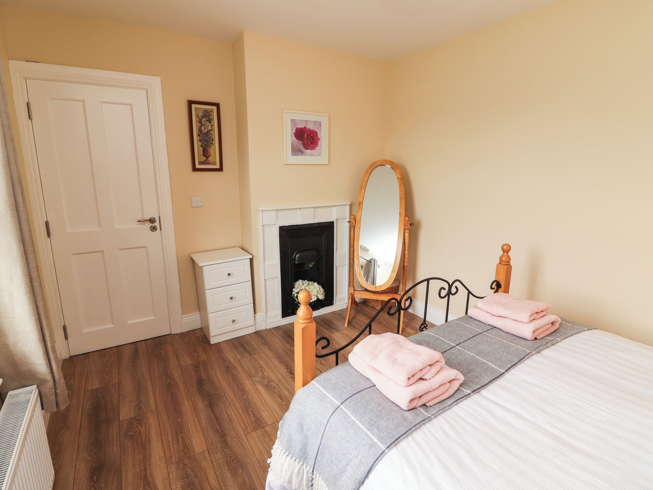 Une chambre à coucher avec un lit, une commode, un miroir, une cheminée et une porte.