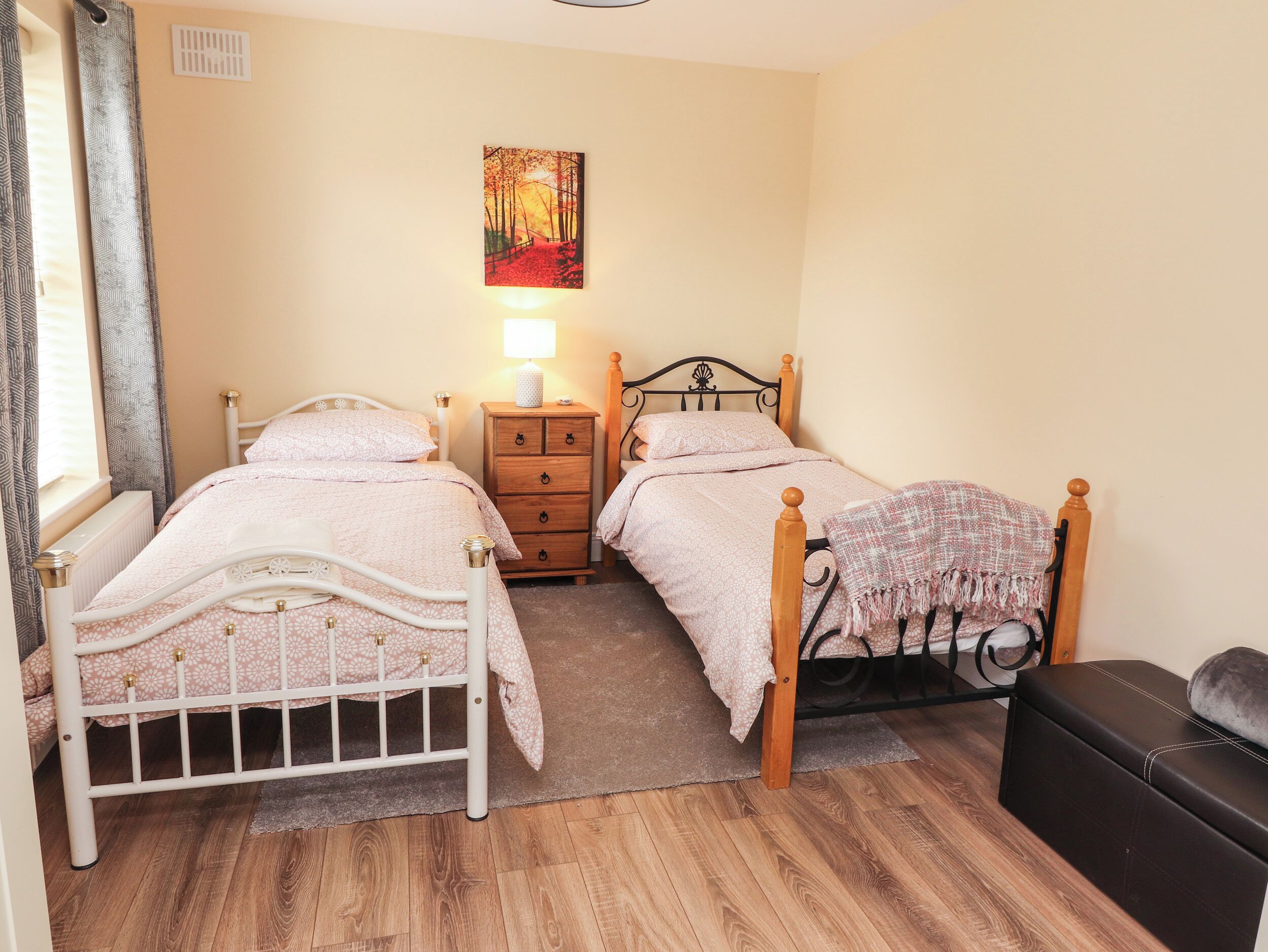 A bedroom with two beds, a wooden dresser, a nightstand with a lamp, and a painting on the wall.