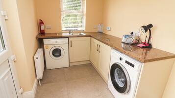 A compact kitchen with a washing machine, a sink, and a window with blinds.
