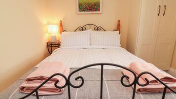 A neatly made bed with pink towels, a bedside lamp, and a painting of a field on the wall.