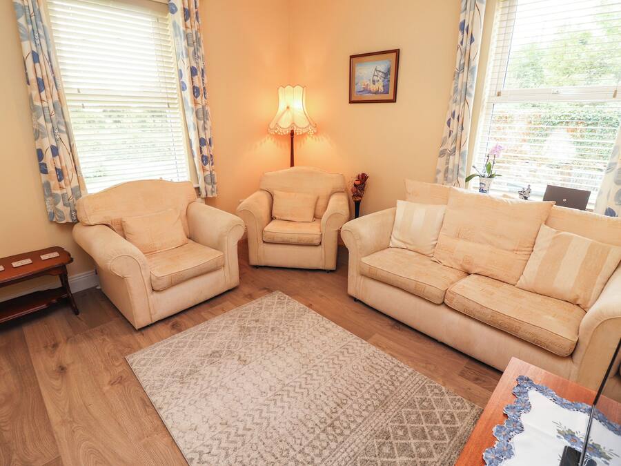 A living room with two armchairs, a sofa, a patterned rug, and a lamp.