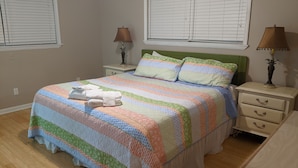 Un dormitorio con cubrecama a rayas, dos lámparas de noche, un cabecero verde y una mesita de noche con cajones.