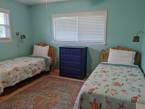 A bedroom with two beds, a dresser, a window with blinds, and a rug.