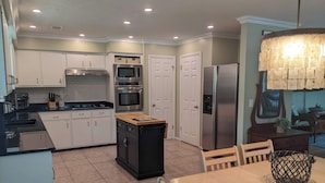 Una cocina moderna con armarios blancos, electrodomésticos de acero inoxidable y un comedor con mesa y sillas.